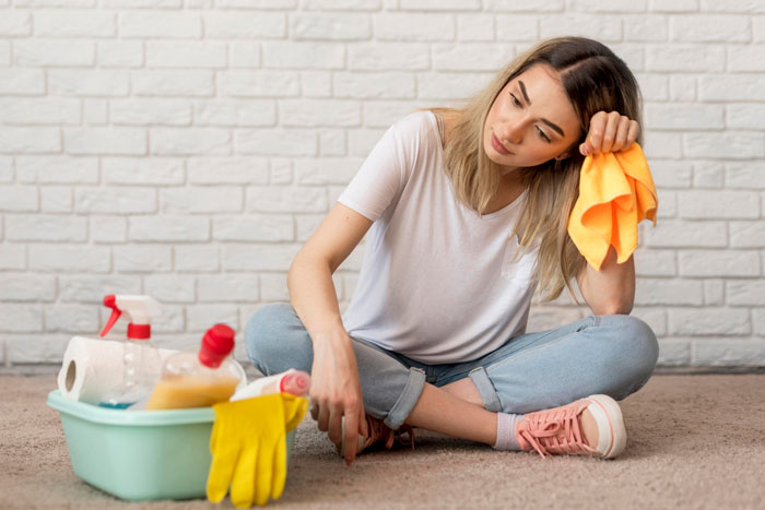 Exhausted mom sitting on floor with cleaning supplies, holding a cloth, overwhelmed by house chores and parenting. Exhausted mom sitting on floor with cleaning supplies, holding a cloth, overwhelmed by house chores and parenting.