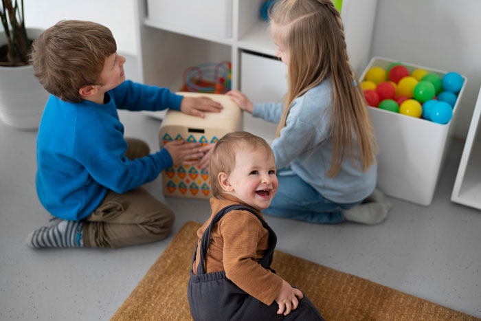 Three young children playing together on the floor in a home environment with colorful toys around them Three young children playing together on the floor in a home environment with colorful toys around them