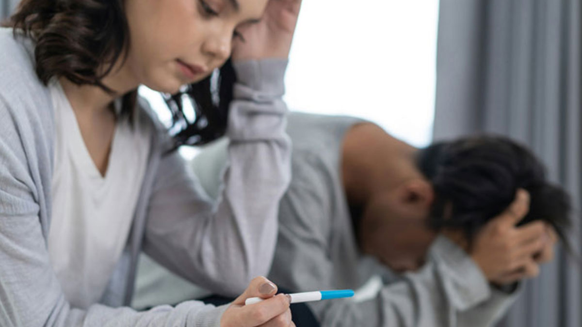 A woman and man sitting apart, both distressed, as she holds a pregnancy test, highlighting family drama adoption conflict.