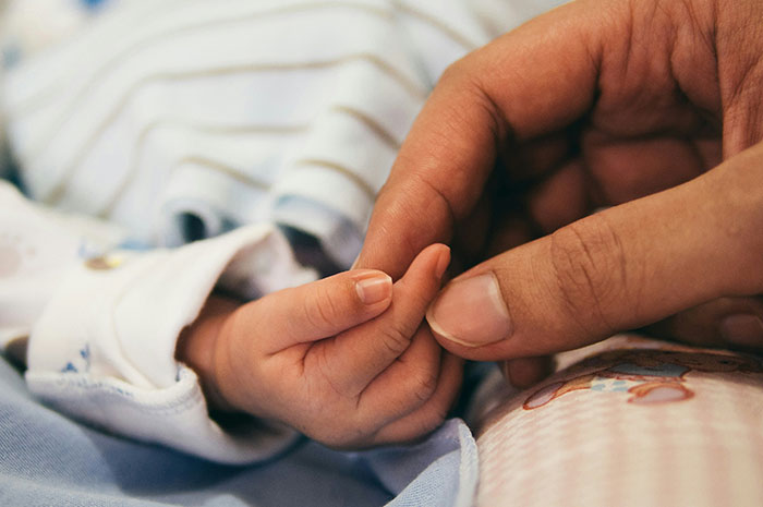 Adult hand gently holding a baby’s hand, illustrating patients googling their symptoms before seeing a doctor.