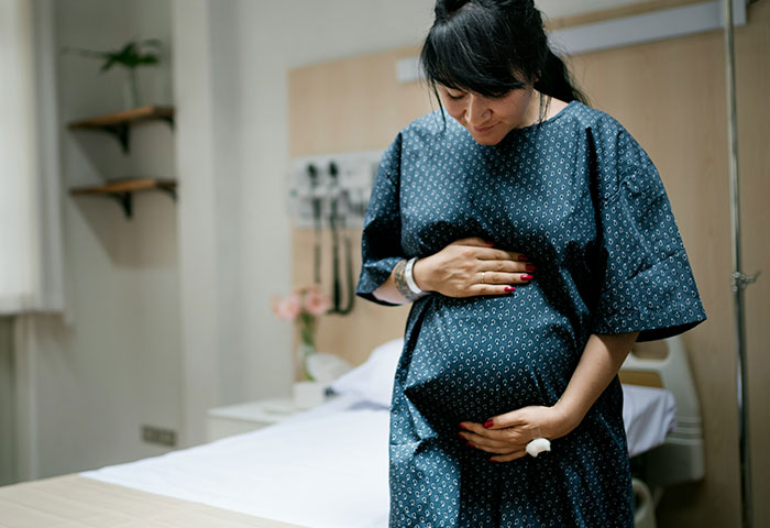 Pregnant woman in hospital gown holding belly, representing doctors witnessing birth meltdowns in delivery room.