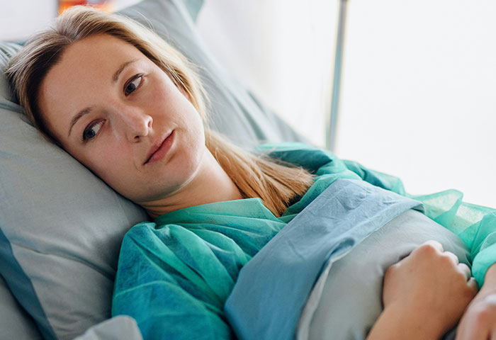 Pregnant woman lying in hospital bed, wearing medical gown, reflecting on birth meltdowns witnessed by doctors.