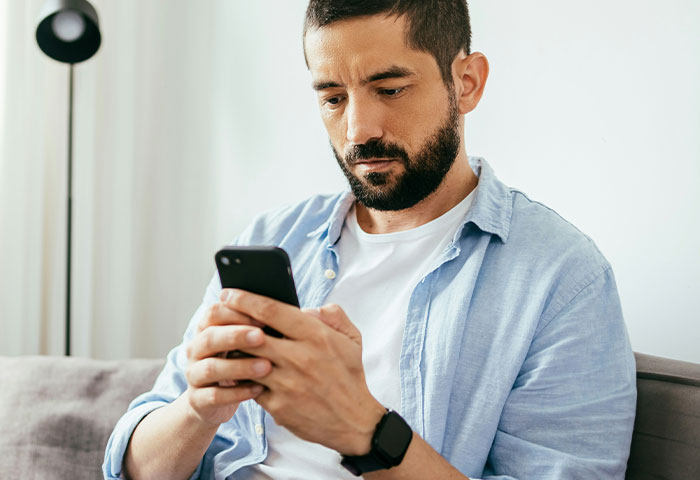 Man with a beard wearing a blue shirt, focused on his smartphone, illustrating doctors witness birth meltdowns concept.