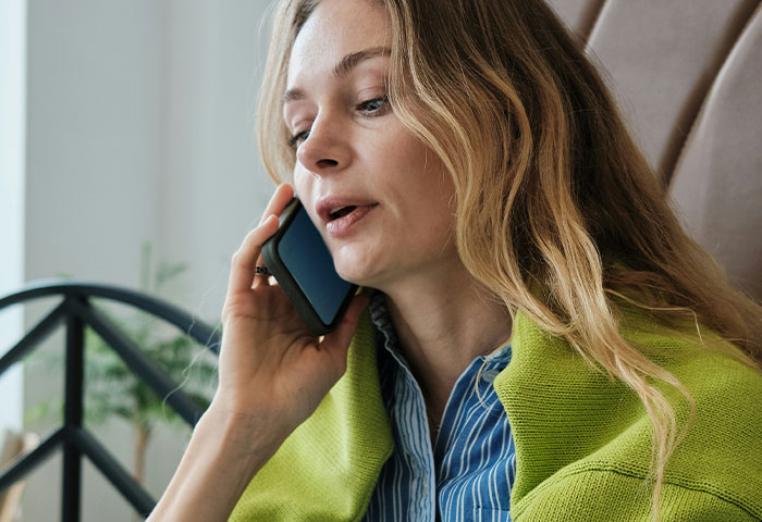 Woman with long hair wearing a green jacket talking on phone, illustrating doctors witnessing birth meltdowns and cheating incidents.