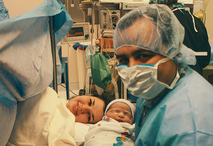 Doctor in scrubs and mask with newborn baby and smiling mother in hospital room after birth meltdown witnessed by doctors.