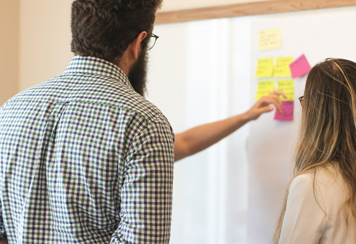 Two professionals brainstorming with sticky notes on a whiteboard, discussing birth meltdowns and cheating cases.