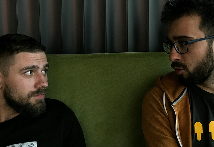Two men with beards having a serious conversation on a green couch, depicting birth meltdowns witnessed by doctors.