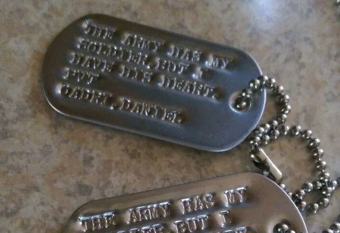 Dog tags with chain laid on a surface, showing embossed text, related to doctors witnessing birth meltdowns and cheating.