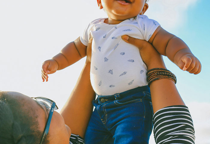 Baby lifted joyfully outdoors by a person, capturing a moment of happiness related to birth meltdowns witnessed by doctors.