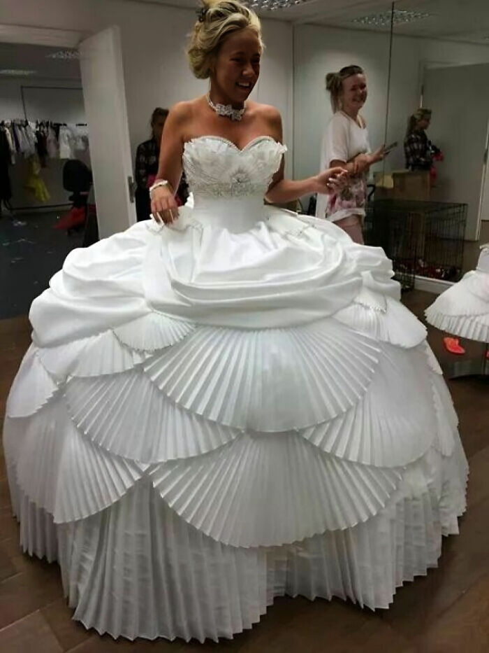 Woman wearing a wedding dress with exaggerated pleated layers and elaborate design, showcasing questionable taste in wedding dresses.
