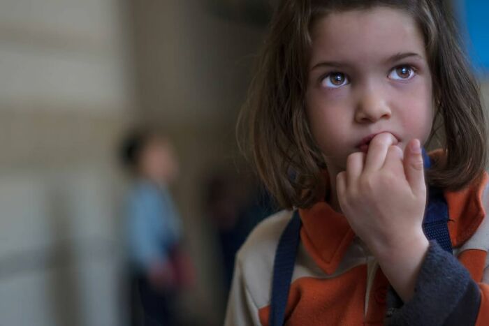Young girl with brown hair, wearing an orange and beige sweater, captured in a beautiful photo of childhood.