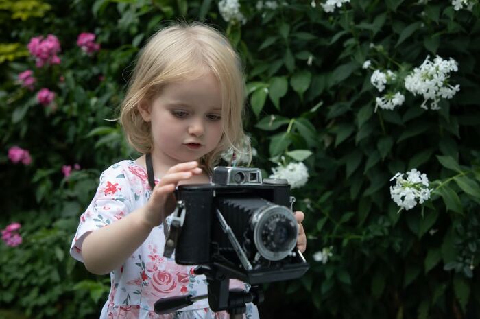 Young child exploring photography with vintage camera outdoors, capturing moments of childhood around the world.