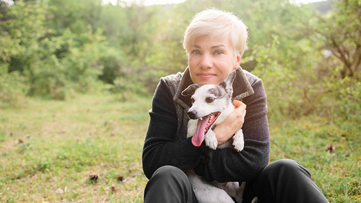 Elderly lady holding small dog outdoors in nature, relating to elderly lady allegedly planning to steal neighboru2019s doggo.