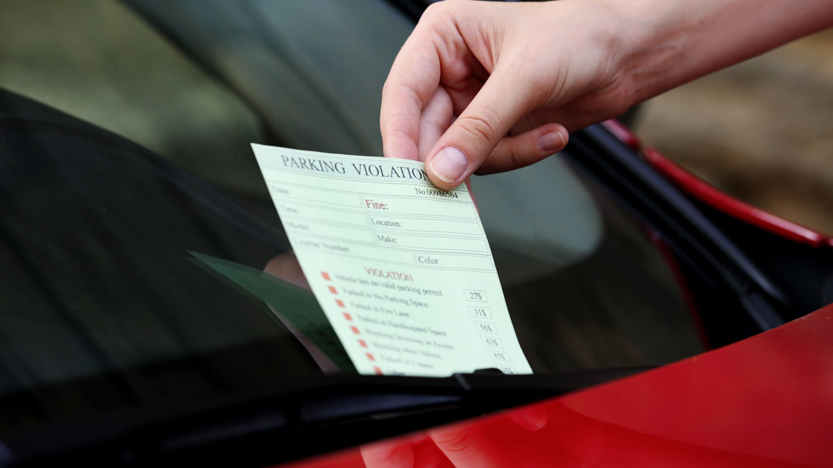 Hand placing a parking violation ticket under a car windshield wiper, illustrating common loopholes to take advantage of.