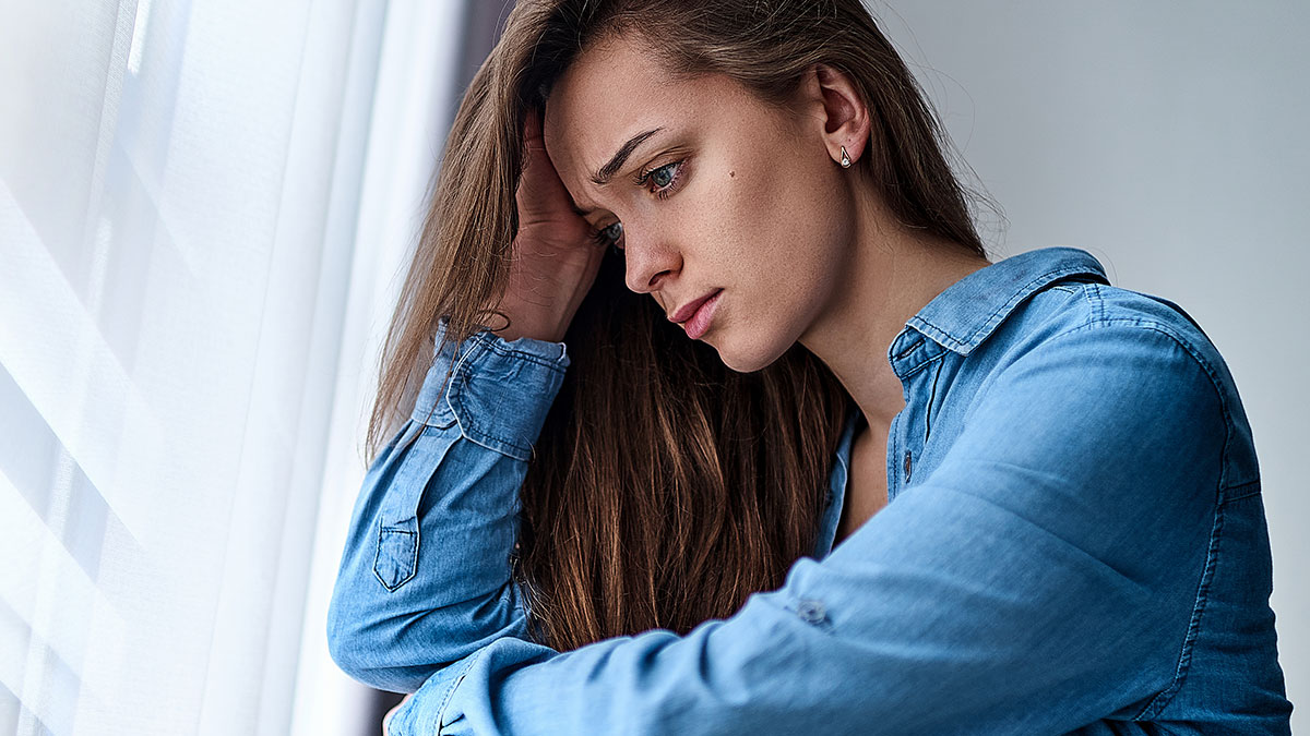 Sad woman in blue shirt looking out the window, reflecting on a man proposing two months after breakup.