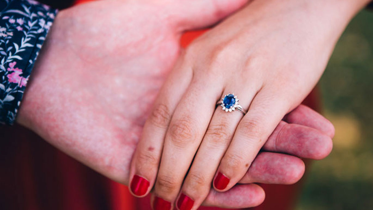 Close-up of two hands holding each other showing a family heirloom ring with a blue gemstone and red nail polish.