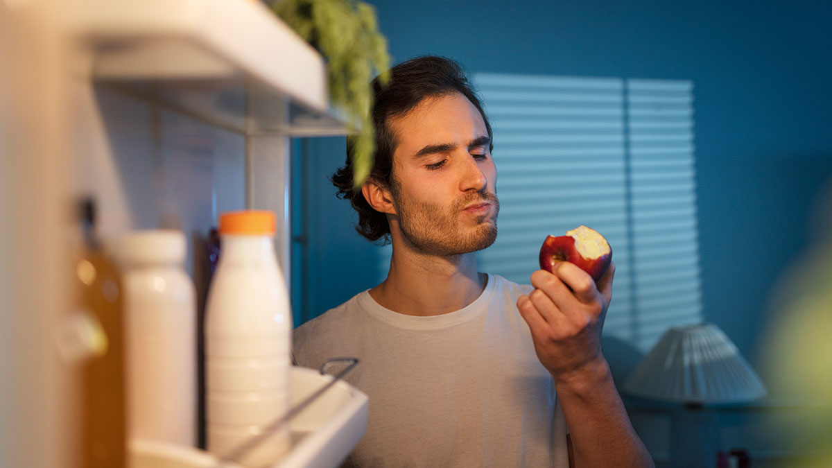 Man eating apple from fridge late at night, illustrating friend who ate everything we owned in a shared home conflict.
