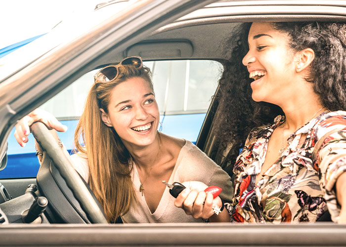 Two women smiling inside a car, one holding car keys, reflecting a family separate drive to Disneyland experience. Two women smiling inside a car, one holding car keys, reflecting a family separate drive to Disneyland experience.
