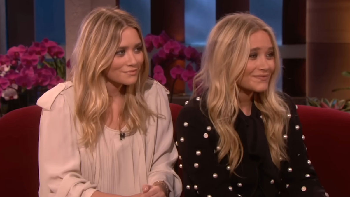 Celebrity twins sitting together on a talk show set with blonde hair and casual stylish outfits, showcasing celebrity twins.