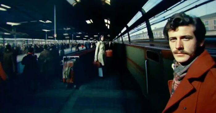 Man in brown coat at train station platform with a woman and travelers, AI recreating childhood memories in biased reality.