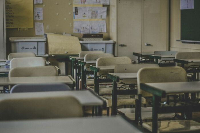 Empty classroom with worn desks and chairs, evoking feelings related to long grudges and unresolved conflicts.
