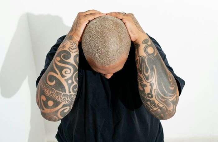 Man with intricate tattoo sleeves holding his shaved head, showcasing bold ink designs and tattoo artist boundaries.