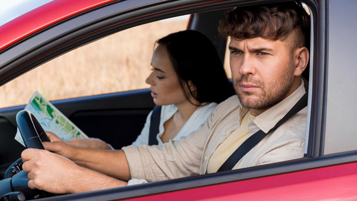Man looking frustrated while driving car with woman reading map beside him, reflecting husband sick of hosting relatives. Man looking frustrated while driving car with woman reading map beside him, reflecting husband sick of hosting relatives.