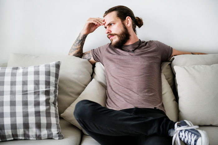 Man sitting on sofa looking frustrated, representing husband sick of hosting wife's distant relatives without thanks. Man sitting on sofa looking frustrated, representing husband sick of hosting wife's distant relatives without thanks.
