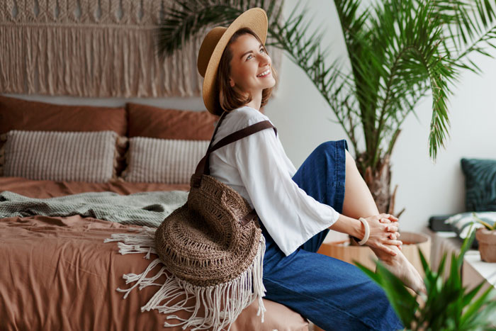 Woman sitting on bed wearing a hat and casual clothes, surrounded by houseplants, symbolizing hosting distant relatives. Woman sitting on bed wearing a hat and casual clothes, surrounded by houseplants, symbolizing hosting distant relatives.