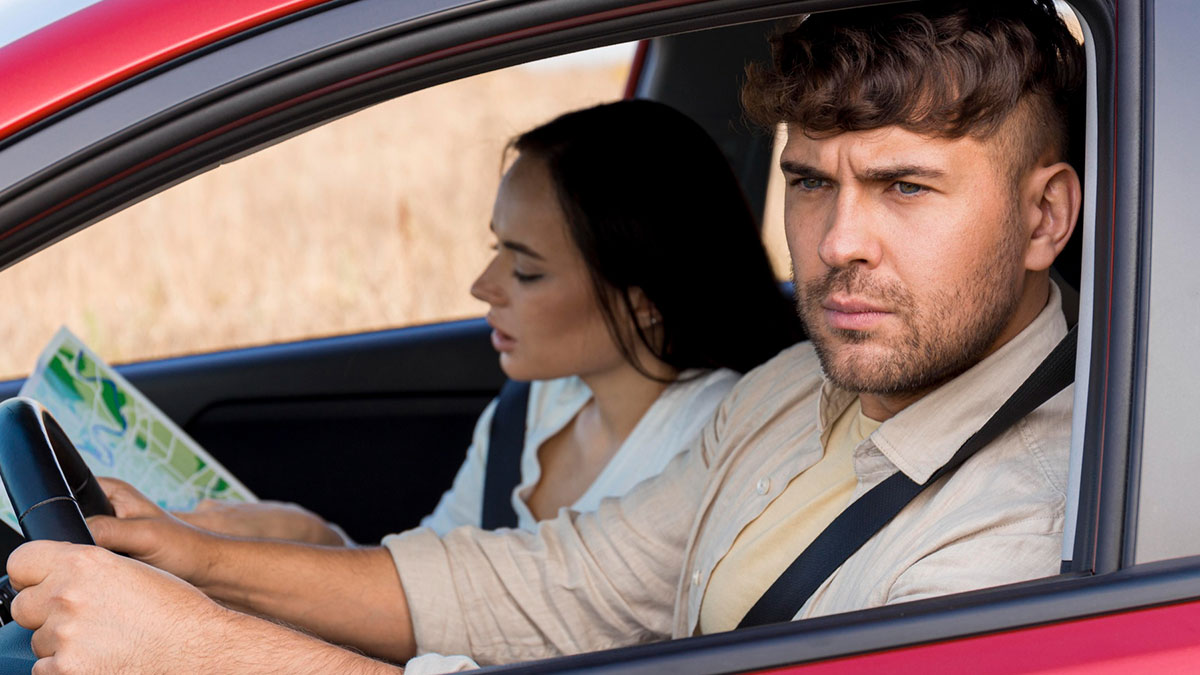 Husband looking upset while driving a car with wife holding a map, reflecting frustration with hosting distant relatives.