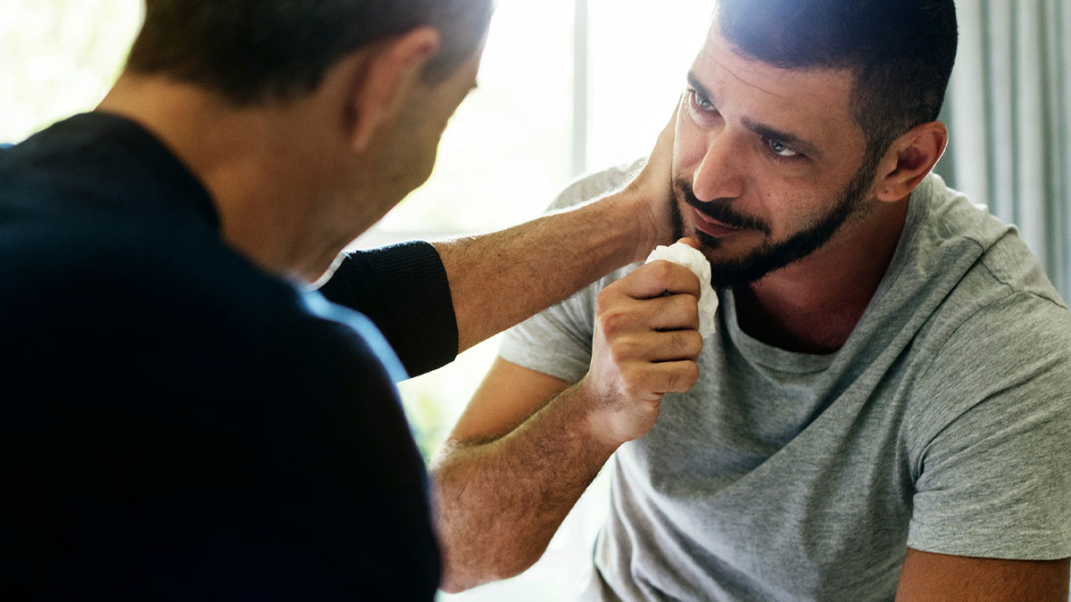 Gay man emotional and devastated, being comforted by another man in a supportive and intimate moment indoors.