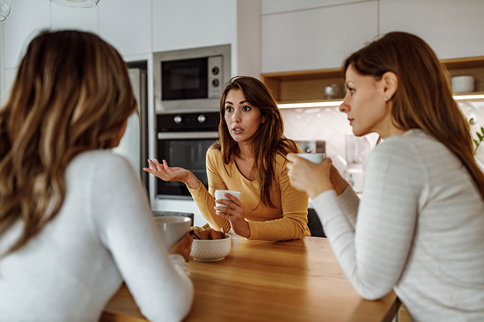 Three women discussing wedding plans in a modern kitchen, capturing a bride getting a reality check about elaborate weddings. Three women discussing wedding plans in a modern kitchen, capturing a bride getting a reality check about elaborate weddings.