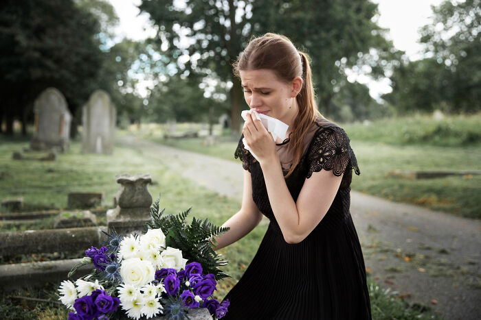 Woman in black dress grieving at a cemetery holding flowers, reflecting the emotions of funeral and family loss. Woman in black dress grieving at a cemetery holding flowers, reflecting the emotions of funeral and family loss.