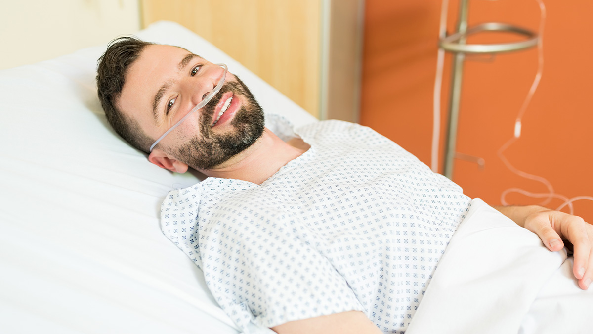 Smiling male patient wearing oxygen tube lying in hospital bed illustrating comical moments medical staff recall in the ER