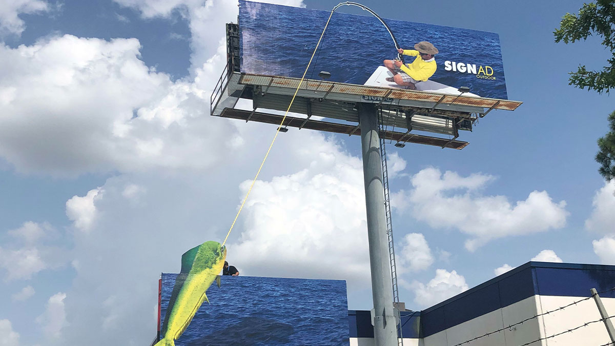 Billboard with a fisherman image and a 3D fish hanging on a rope, showcasing funny and weird billboards outdoors.