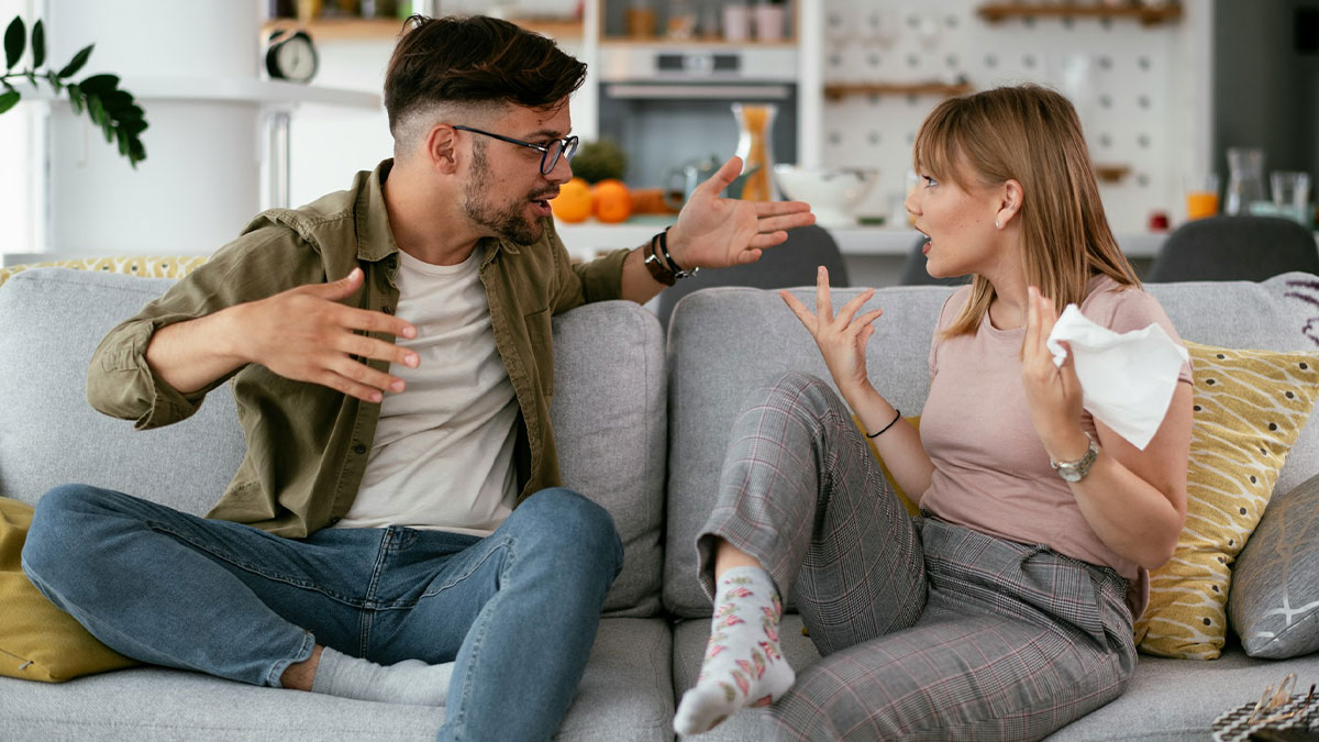 Young man and woman having an intense argument on a couch, illustrating really dumb tweets causing frustration or disbelief.