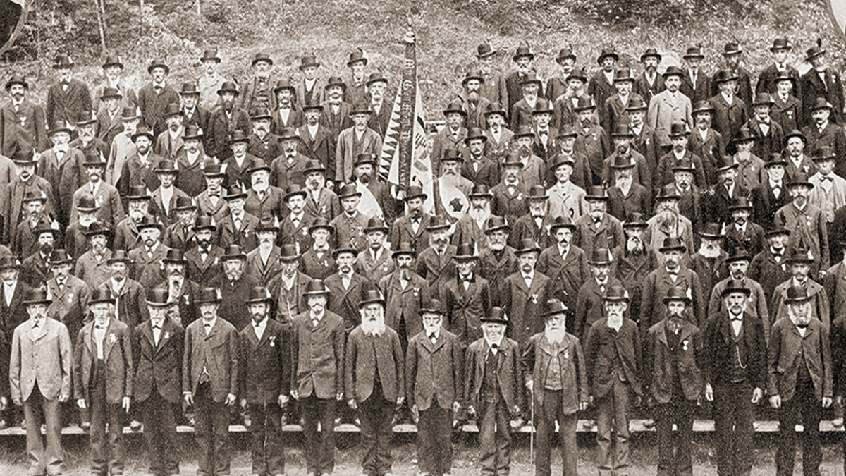 Large group of men in vintage suits and hats posing outdoors for a historic photo capturing events from history that will never be funny