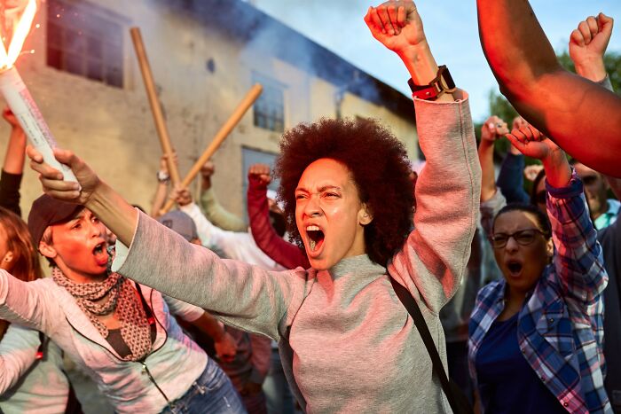 A diverse group of people raising fists and shouting passionately, depicting positive stereotypes about various countries.