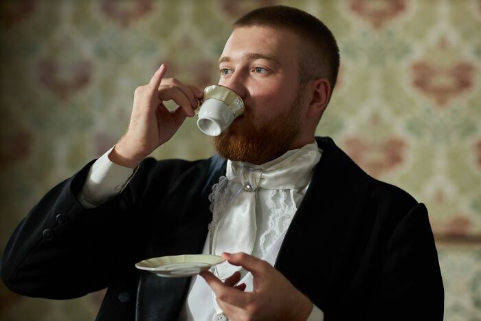 Young man in vintage clothing drinking tea, illustrating positive stereotypes people have about various countries.