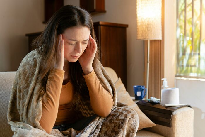 Woman wrapped in blanket holding her head in discomfort, illustrating first opinions doctors often hear from patients.