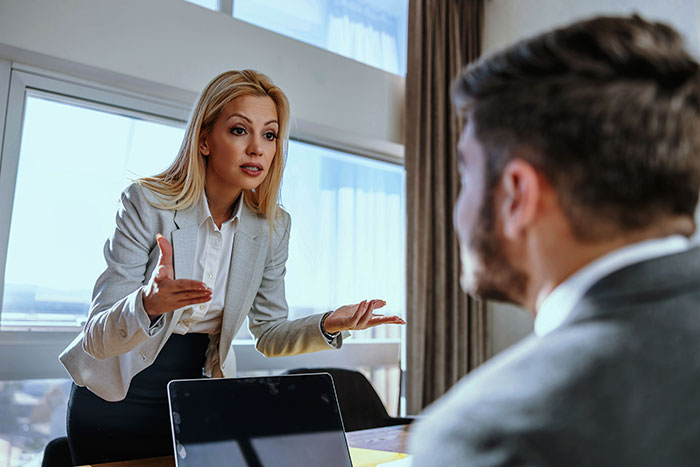 Woman in business attire talking to a seated man shutting down younger coworker flirt in a modern office setting