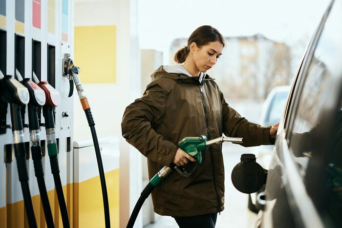 Woman using genius life hacks while fueling her car at a gas station, realizing extra work in daily tasks.