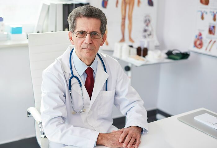 Doctor wearing glasses and white coat with stethoscope sitting in medical office, representing worst first opinions heard by doctors.