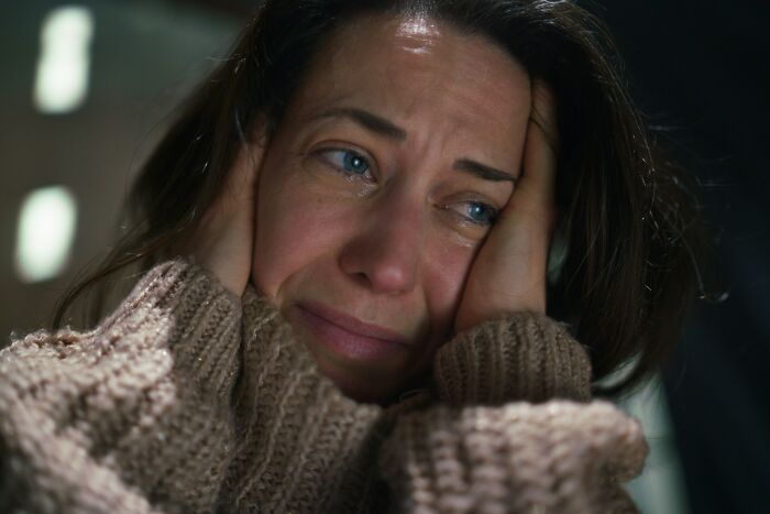 Woman in a brown sweater covering ears and crying, illustrating emotional impact of shocking things popular kids did in school outcasts