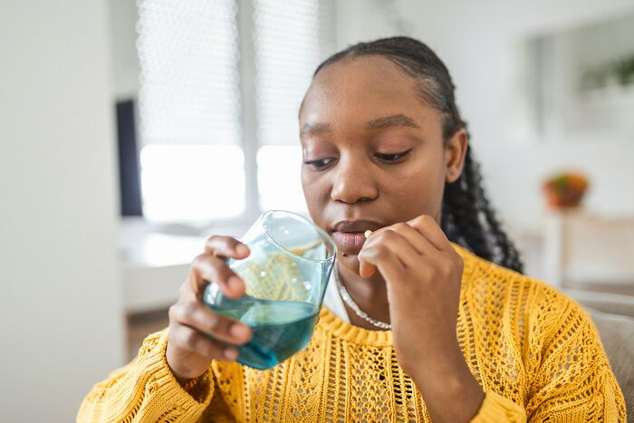 Woman in yellow sweater about to take medication with a glass of water, illustrating doctor first opinions on health issues.