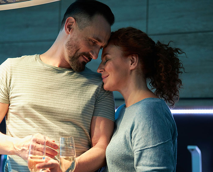 Couple sharing a tender moment indoors with drinks, highlighting husband unattracted plastic surgery wife relationship tensions. Couple sharing a tender moment indoors with drinks, highlighting husband unattracted plastic surgery wife relationship tensions.