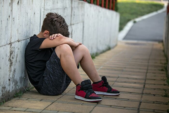 Young boy sitting alone against a wall looking upset, illustrating popular kids turning into outcasts in school.