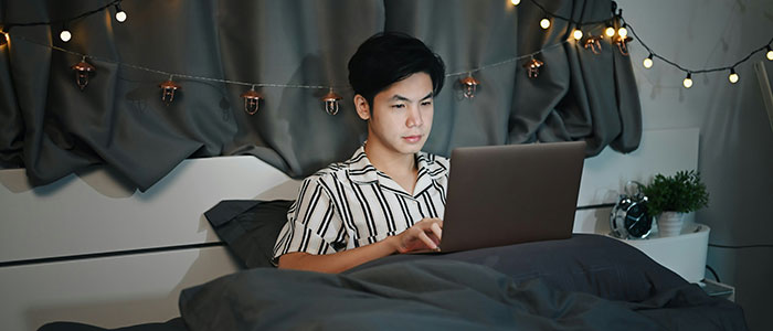 Young man in striped shirt in bed at night, looking concerned while using laptop, hinting at creepy secret photos discovery. Young man in striped shirt in bed at night, looking concerned while using laptop, hinting at creepy secret photos discovery.
