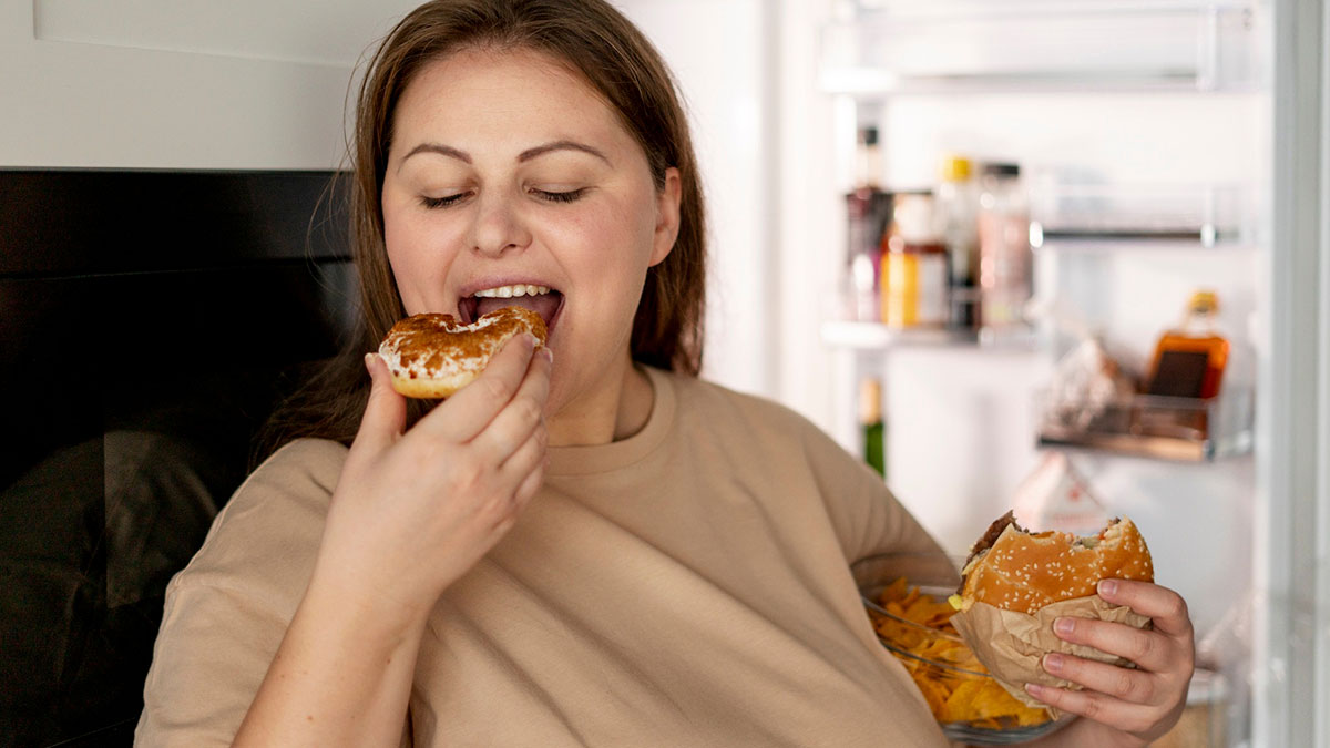 Woman eating food from fridge holding burger and chips, illustrating drama over brou2019s girlfriend eating food.