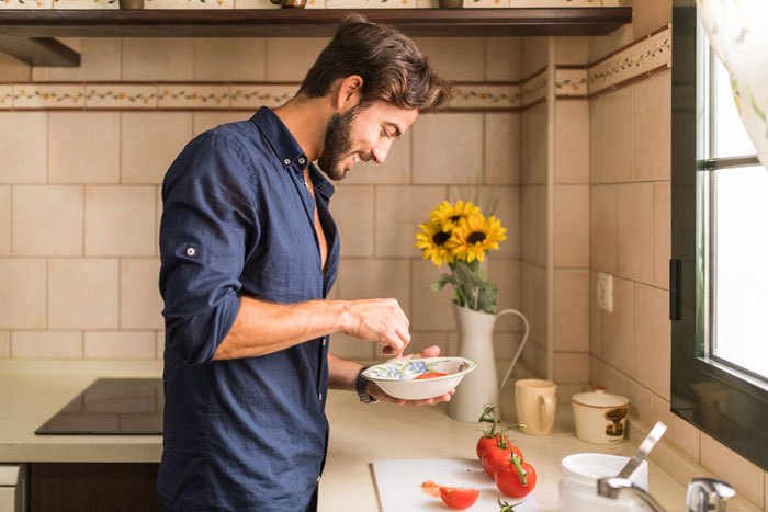 Stay-at-home boyfriend in kitchen preparing food, embodying intelligence and kindness as described by proud woman supporter.